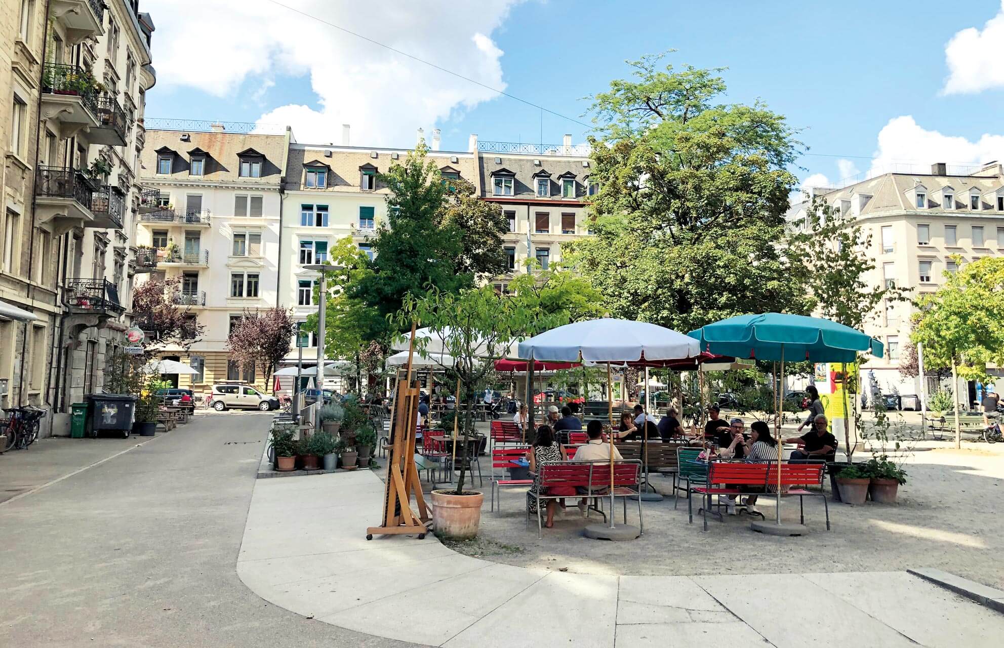Personen sitzen unter Sonnenschirmen im Café auf dem Idaplatz.